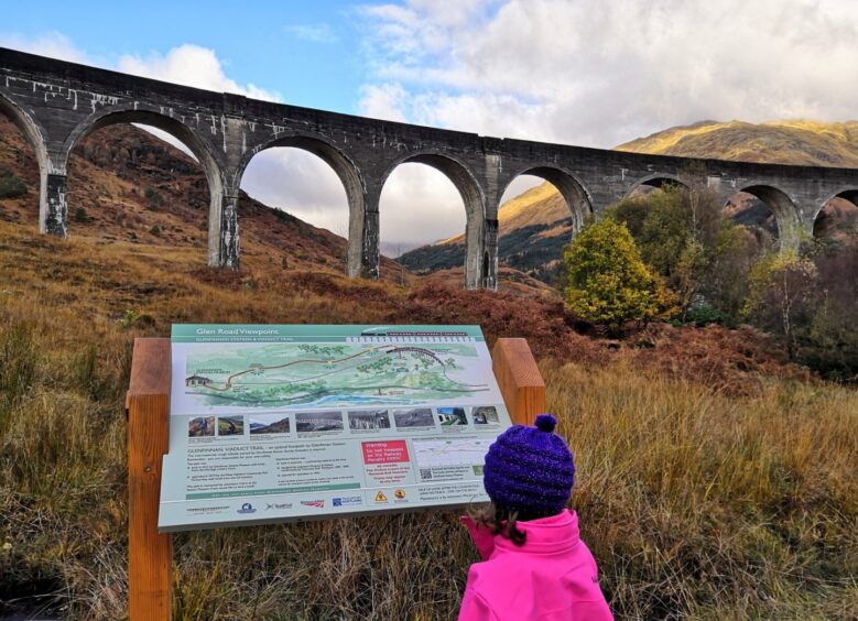 child looking at a notice board at the Glenfinnan monumnet. 