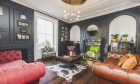 Living room with high ceilings, ornate plasterwork, lime-green tiled fireplace, and panelled walls and wooden floor