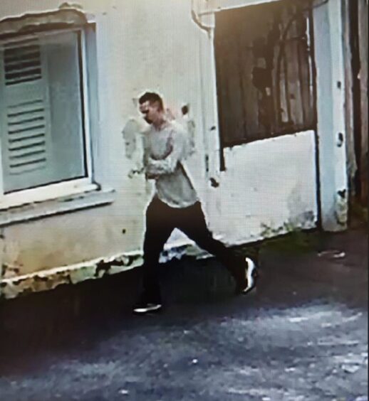 CCTV footage of Alexsandr dressed in hoodie and jeans walking by white building.