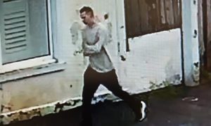 CCTV footage of Alexsandr dressed in hoodie and jeans walking by white building.