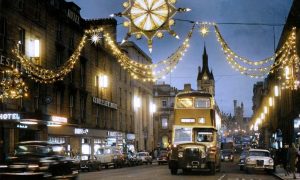 1964: Reimagined in colour for the first time, the Christmas lights give Union Street a softer ambiance, and the AI colourisation has correctly picked up the Aberdeen Corporation colours of cream and green for the bus. This image was taken outside Falconers, now occupied by Evans Cycles, near the junction of Union Street and Market Street. Image: DC Thomson