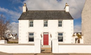 The outside of The Dipping Lugger restaurant, housed within charming house with red door, white walls and white wall.