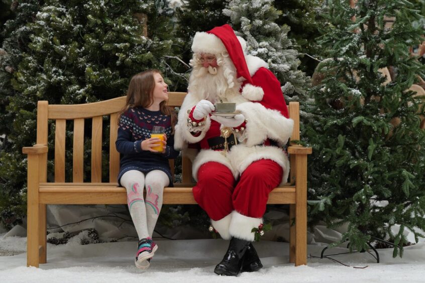 A little girl sitting on a bench with Santa