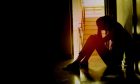 Silhouette of a sad young girl sitting in the dark leaning against the wall.