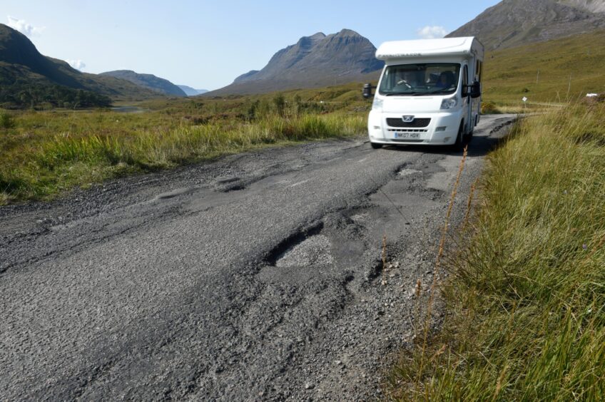 Motorhome driving along single track road with potholes.