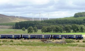 View of Scotrail train travelling along railway line with fields and hills in the background.