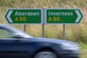 Busy traffic speeding past Inverness and Aberdeen sign posts on the A96 at Gollanfield between Inverness and Nairn.