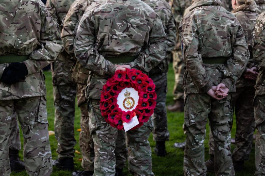 Soldier holding poppy wreath behind his back