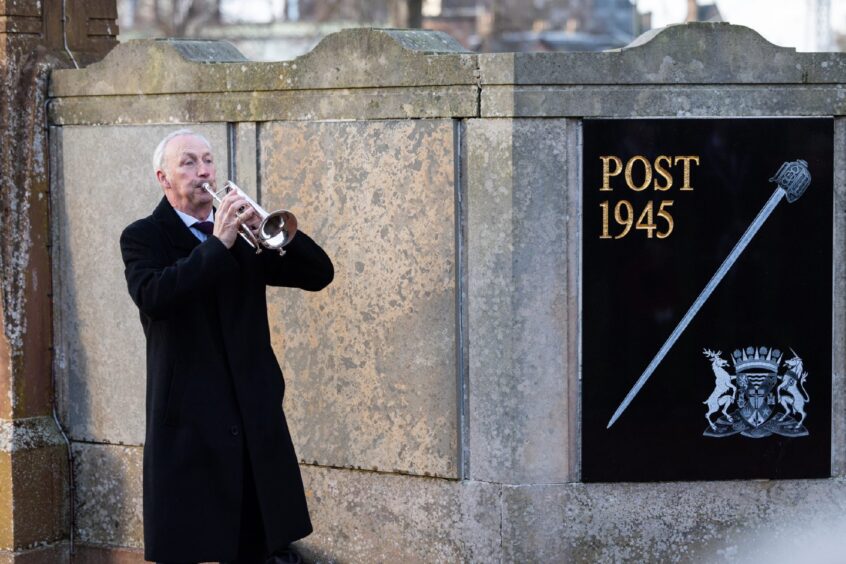 Man in black coat plays horn next to memorial 