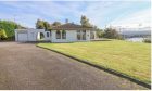 White bungalow on the crest of the brae surrounded by green grass and the Kessock Bridge in the distance.