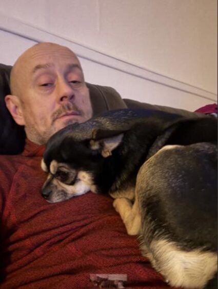 Black chihuahua lies on the chest of owner Kev Stewart wearing burgundy top.