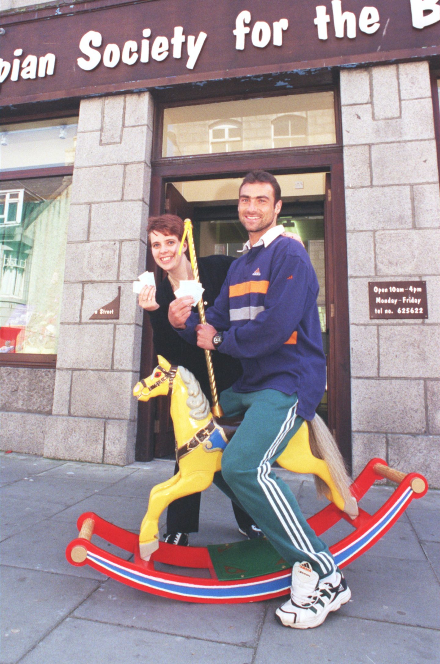 Aberdeen midfielder Andreas Mayer astride a rocking horse as he picks out the winning ticket at an event for Grampian Society for the Blind alongside Debbie Cran.