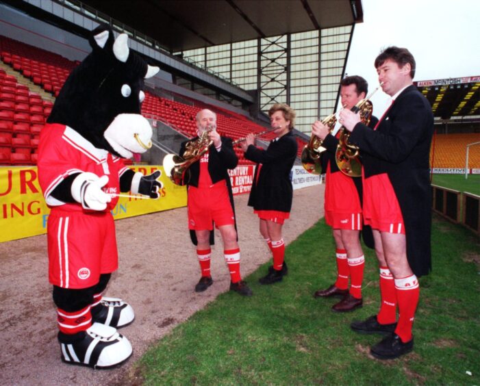 Musicians from the Royal Scottish National Orchestra play their instruments in Aberdeen FC kit while Angus the Bull conducts them