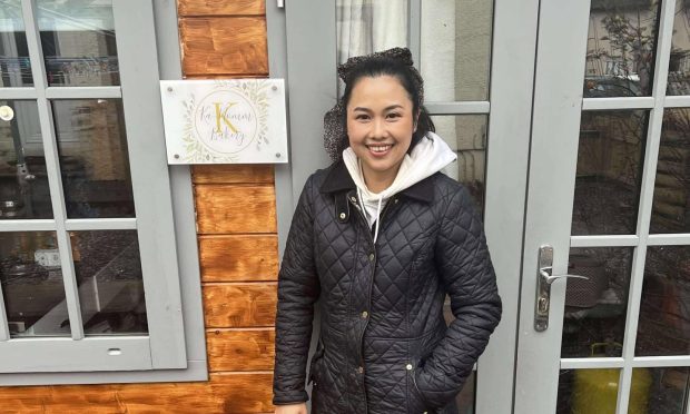 Gift Hardwick wearing a black jacket in front of her wooden summer house with grey painted window frames.