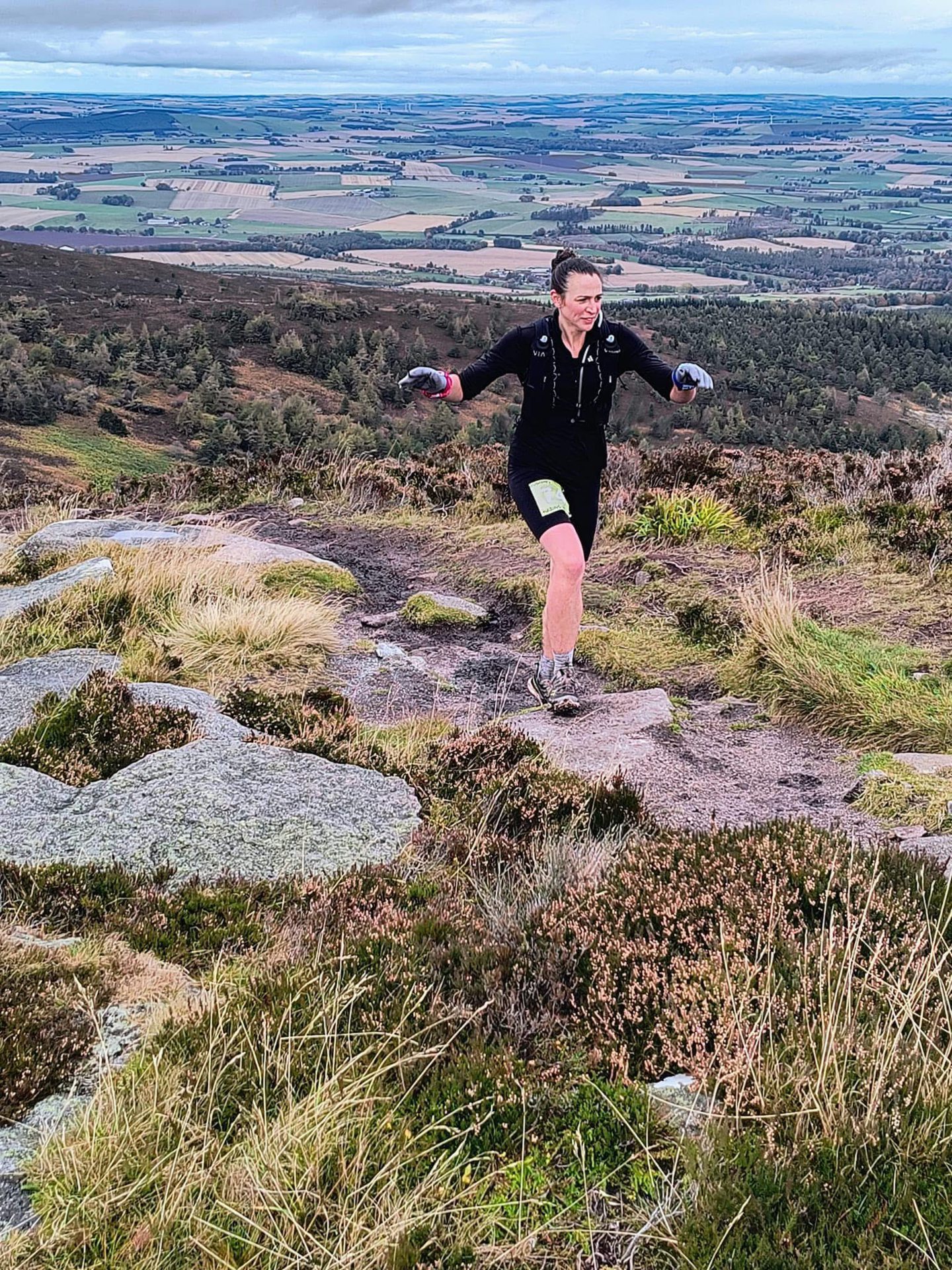 a runner high on a hillside with fields below stretching into the distance 