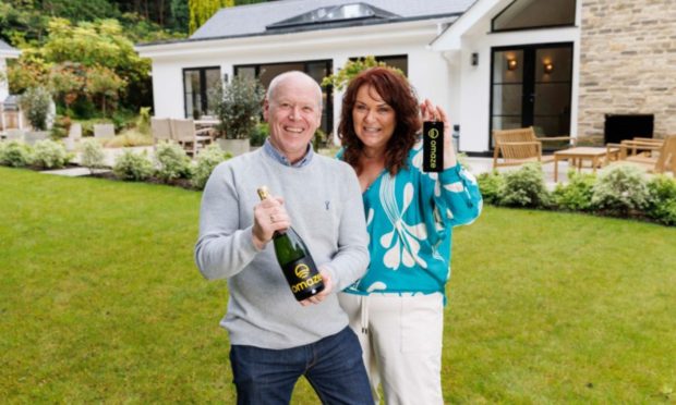 Rachael and Darren Reid, hold a bottle of champagne and key on the grounds of £3 million Surrey Home,