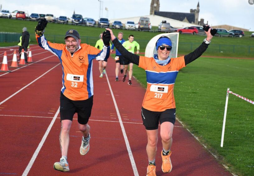 two runners with their arms aloft cross the finish on a line running track at the Fraserburgh Half Marathon