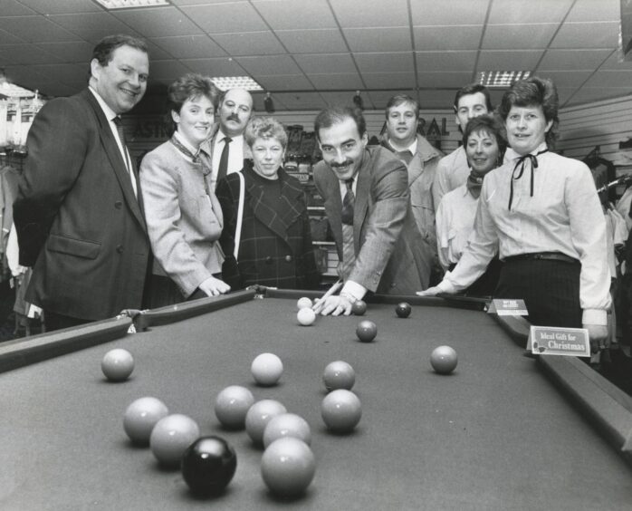 Aberdeen legend Willie Miller lines up a shot on a snooker table at the new Astral Sports section of the city's Frasers department store on 10 December 1987. Store manager Miles Paterson and Astral Sports manageress Mrs Debby Grant are on the left.