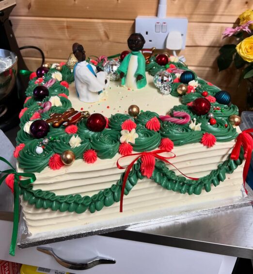 Figurines of Nigerian ministers Father Maximilian Nwosu, CCE and Father James Anyaegbu, CCE, priests at nearby St. Mary Catholic Church in Beauly, on top of a white square cake decorated with green and red icing.