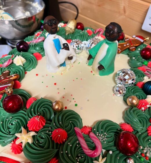 Figurines of Nigerian ministers Father Maximilian Nwosu, CCE and Father James Anyaegbu, CCE, priests at nearby St. Mary Catholic Church in Beauly, on top of a white square cake decorated with green and red icing.