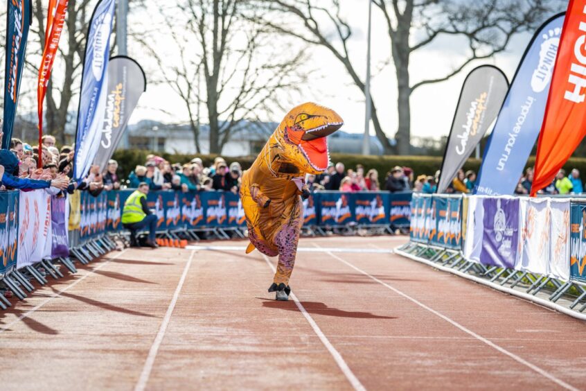 a runner in a dinosaur costume approaches the finish line in the Inverness half marathon