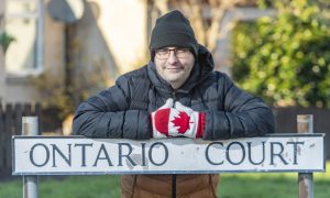 David Mackay leaning on Ontario Court sign wearing Canadian gloves.