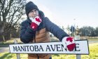 David Mackay leaning on Manitoba Avenue sign wearing Canadian gloves.