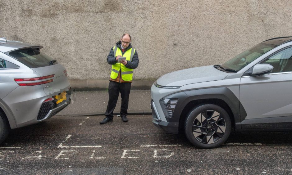 Reporter David Mackay with notepad next to cars in disabled bays.