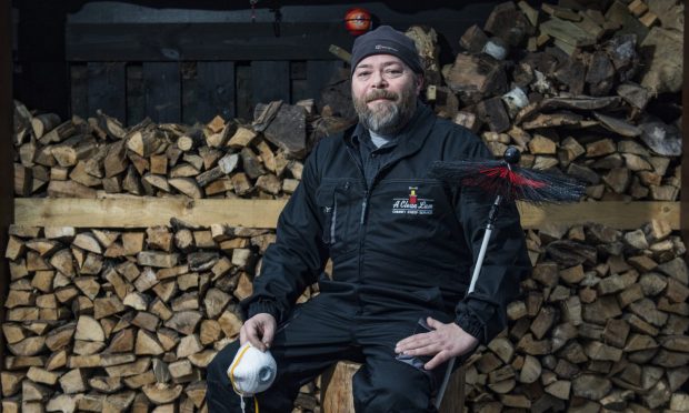 Stafford Turnidge sitting with chimney brush in front of firewood.