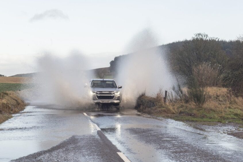 Car driving through puddle causing spray on both sides of the vehicle.