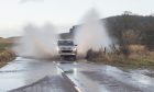 Car driving through puddle causing spray on both sides of the vehicle.