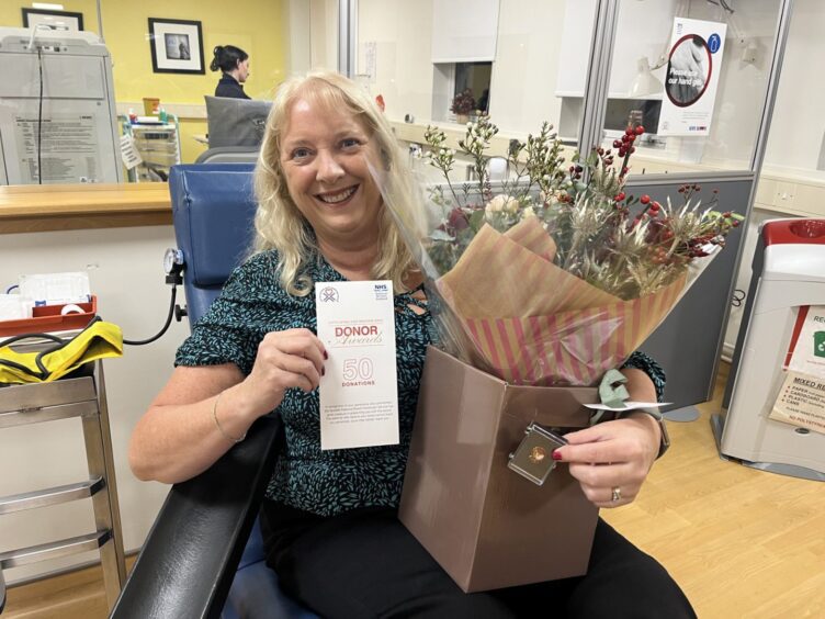 Joanna Blake holding 50th donor card and bouquet of flowers