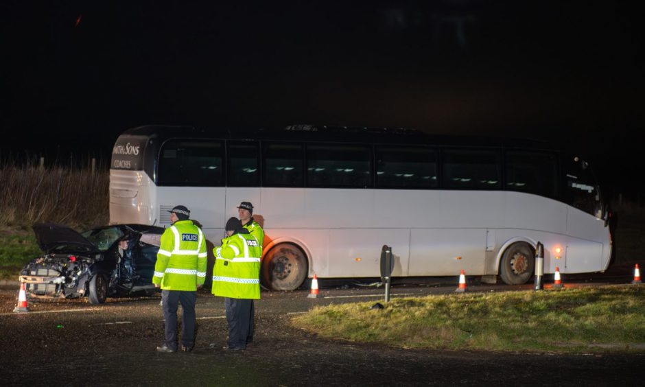 White bus with black car at the rear cordoned off by cones.