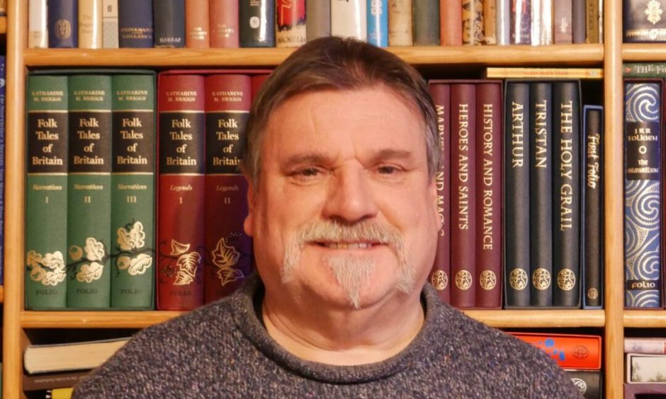 Tom Muir smiling in front of book case.