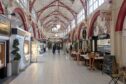 View of interioer of Inverness Victorian Market with red beams on the ceiling and shops on each side.