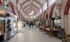 View of interioer of Inverness Victorian Market with red beams on the ceiling and shops on each side.