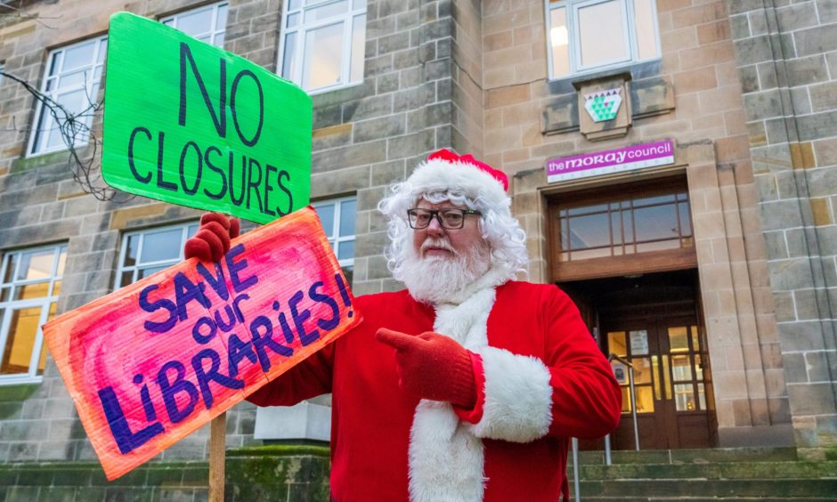 Santa holding signs protesting library closures. 