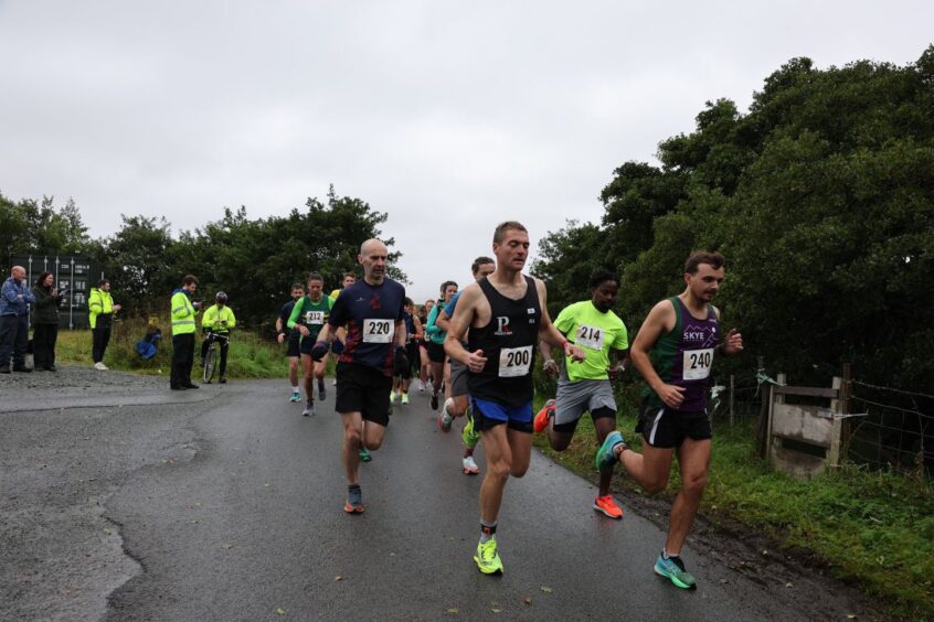 runners on a road with trees on either side and stewards looking on