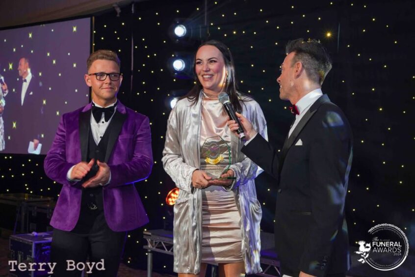 Susan Smart on stage with a gentleman on each side accepting her award.