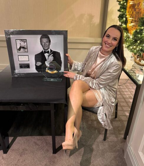 Susan smart sitting with her leg crossed at a table with her award and a signed 007 picture.