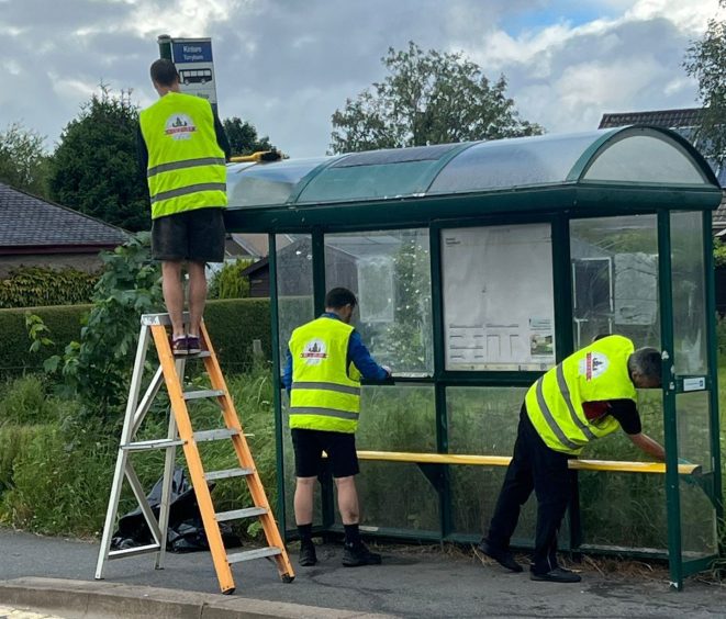 Volunteers giving a bus shelter a clean and tidy.