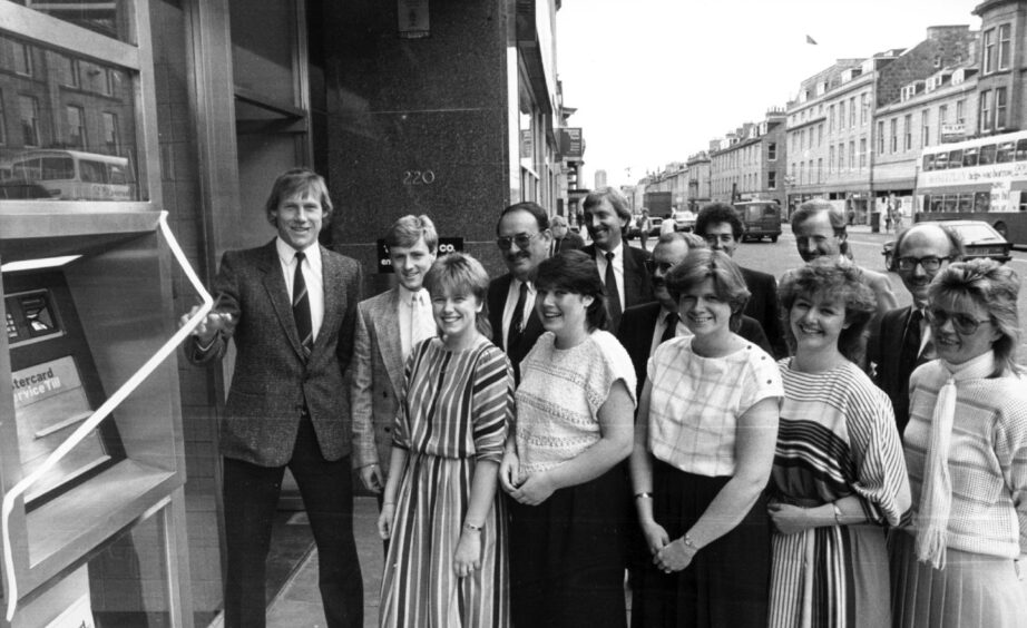 Aberdeen FC star Doug Rougvie has the honour of cutting the tape to open the first building society cash machine in Aberdeen at the Leicester Building Society office on Union Street in 1984. Team-mate Stewart McKimmie, second left, and staff look on.