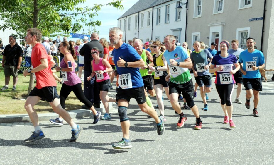 runners round a bend in the road, with houses in the background 