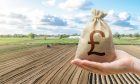 Hand with British pound sterling and a farmer on a tractor works on farm field.