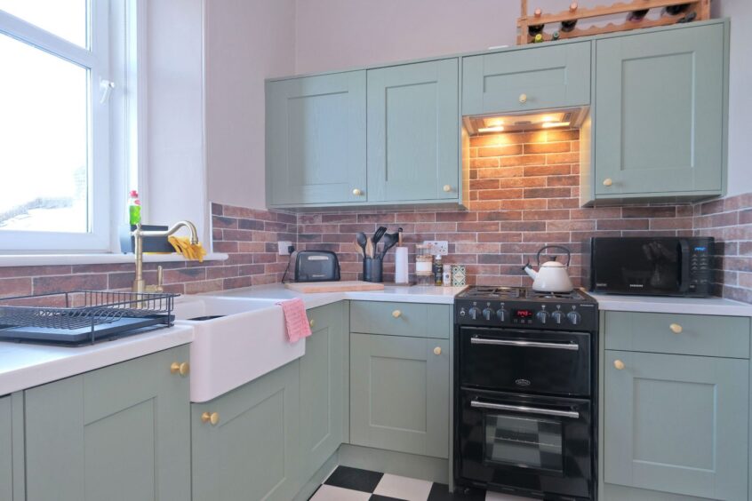 kitchen with green units and exposed brick splashbacks