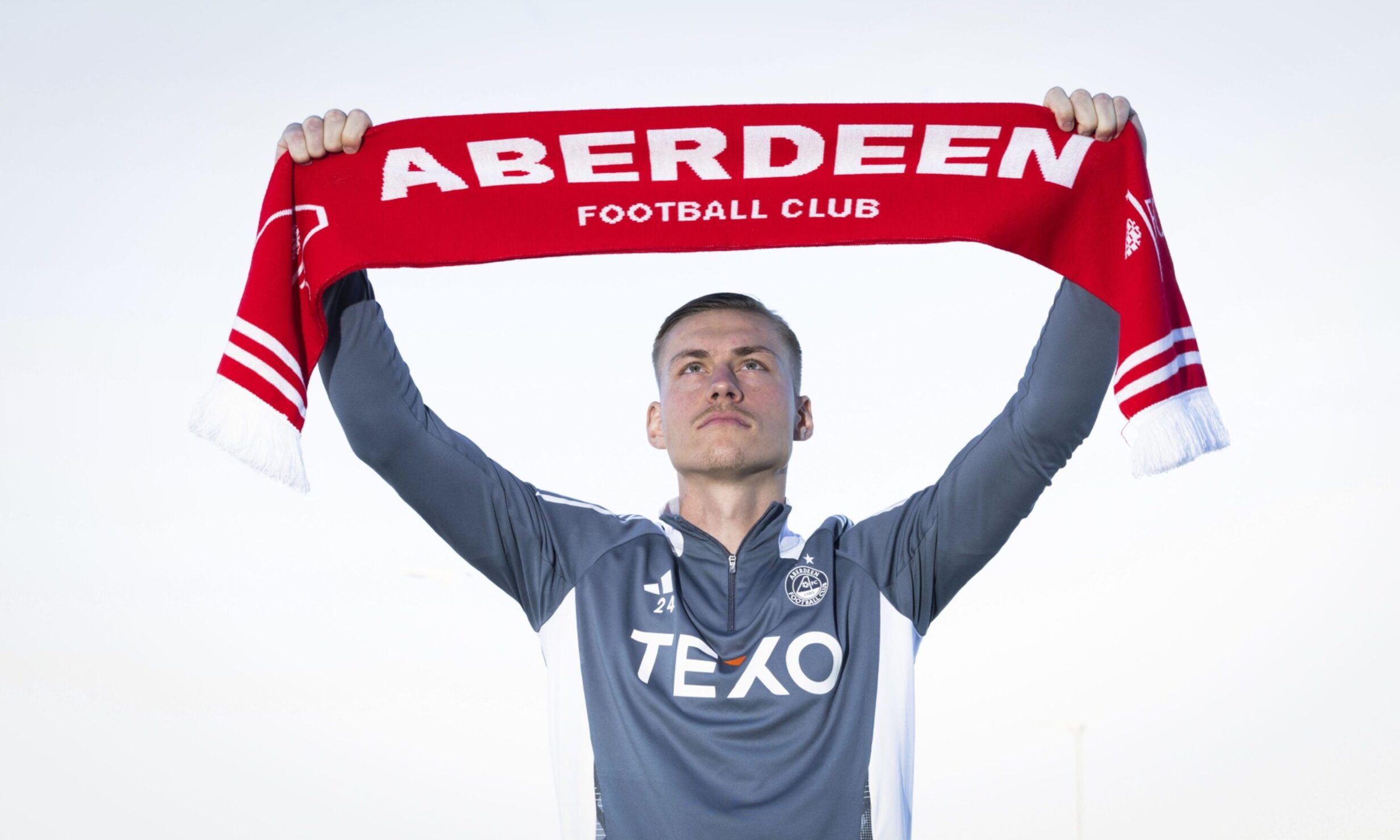 Kristers Tobers holds aloft an Aberdeen scarf. Image: SNS.