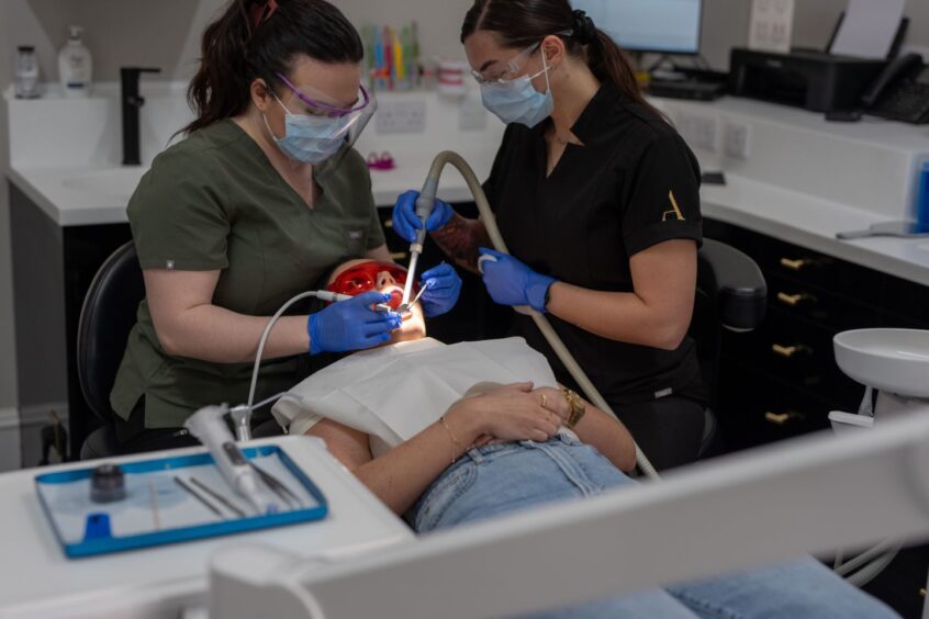 patient lies down as dentists use tools to check on her oral health