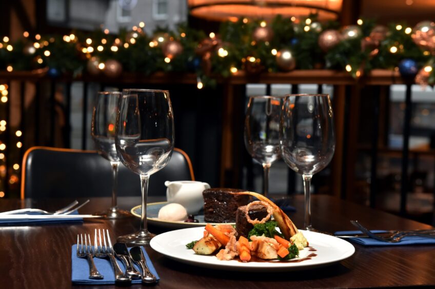 A dining table with gourmet food, wine glasses, and holiday decorations in the background.