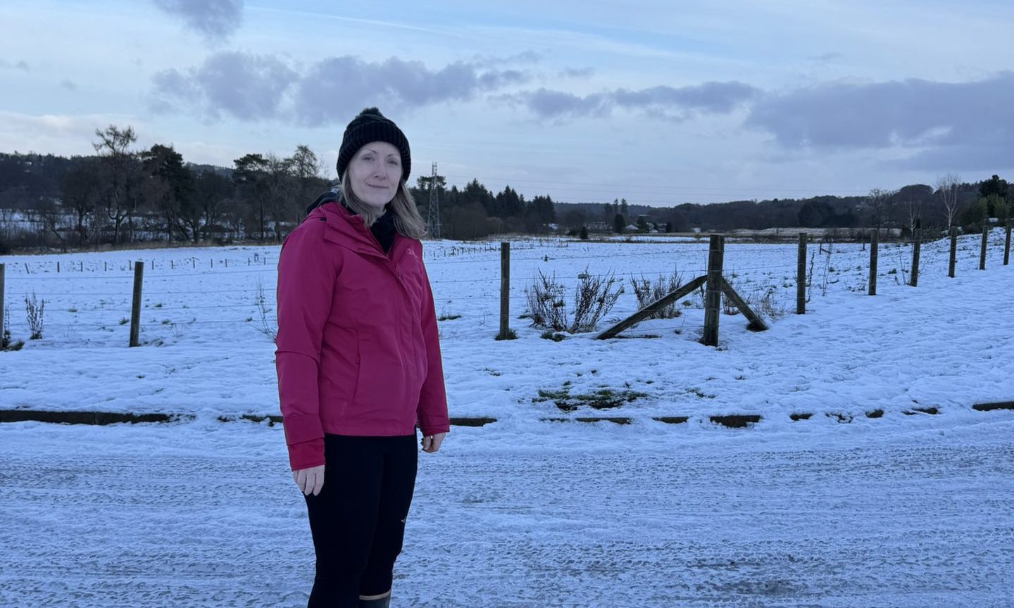 Tara Zacha in a pink jacket and hat in front of field covered in snow.