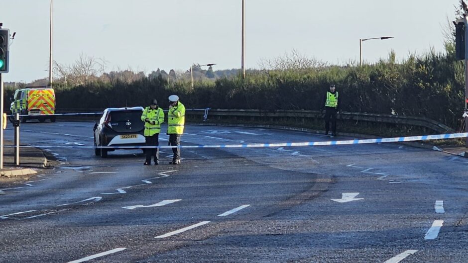 Police officers stand behind a tape cordon as they investigate the crash scene, near to the Inshes roundabout in Inverness